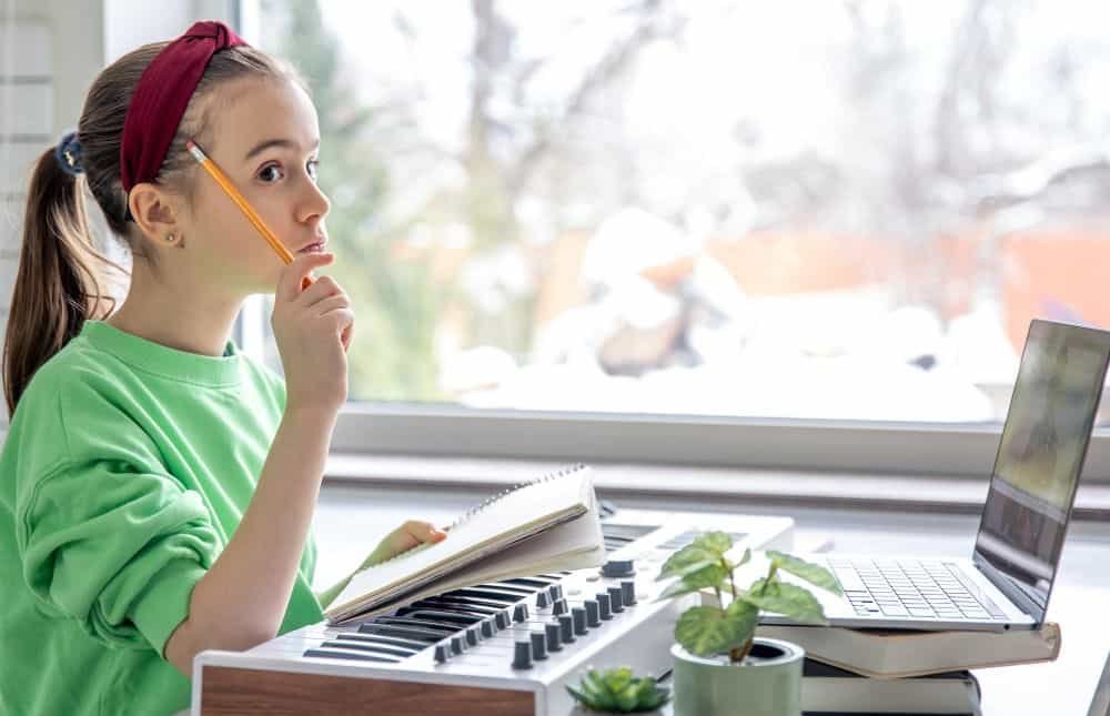Foto de una niña delante de un piano pensando con una libreta y un lapiz